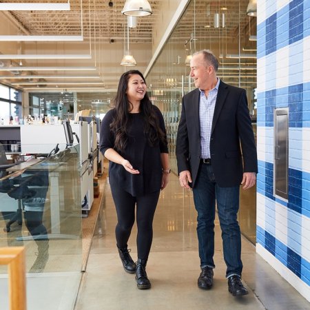 Two people walking and talking in an office setting.