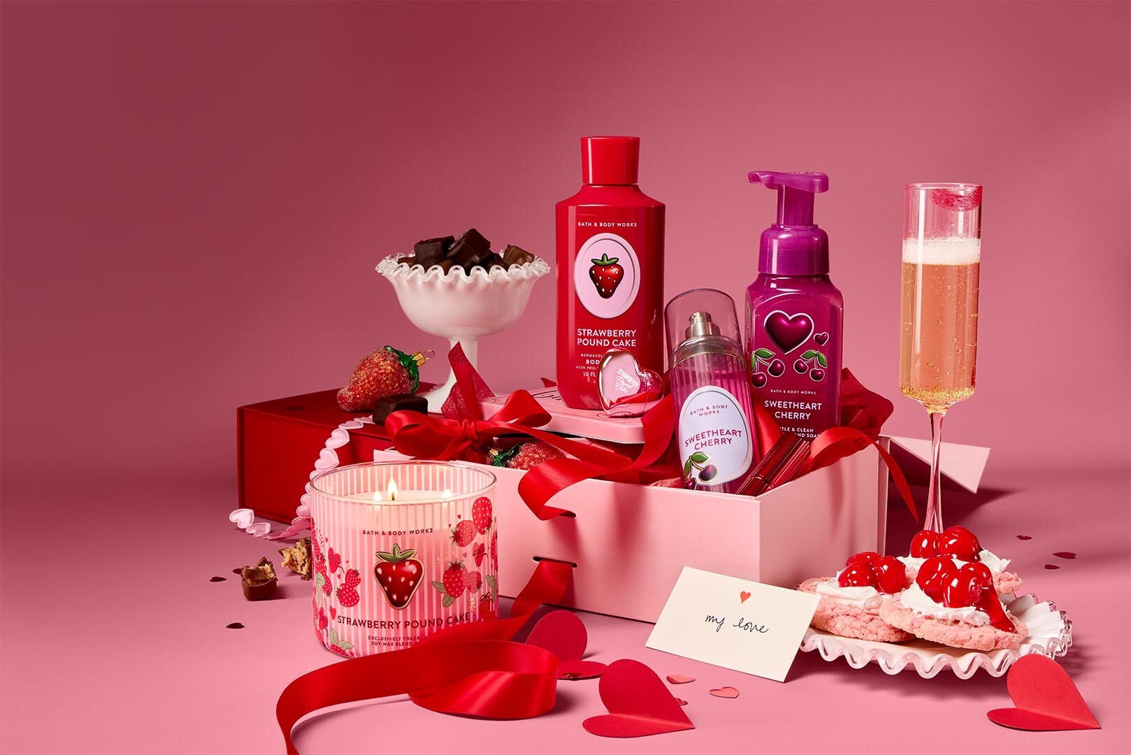 Photo of Bath & Body Works Valentine's Day products in a pink box surrounded by treats and champagne